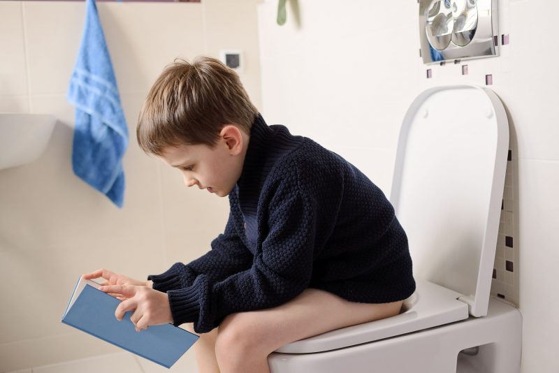 djedzura160100129.jpg - little 6 year old boy sitting on the toilet and reading a blue book