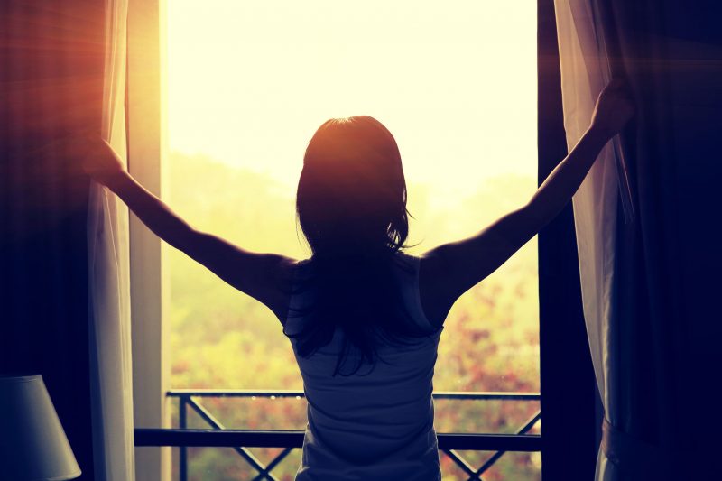 窓を開けて太陽の光を浴びる女性