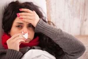 yacobchuk150100377.jpg - flu. closeup image of frustrated sick woman with red nose lying in bed in thick scarf holding tissue by her nose and touching her head