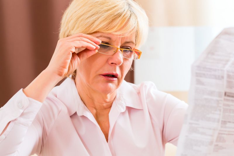 メガネをかけて新聞を読む白人女性の画像