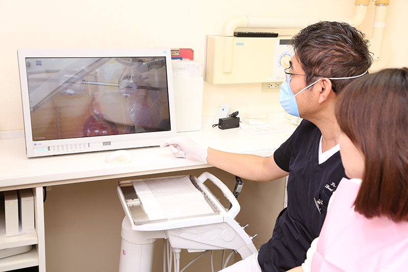 マイクロスコープの画像を見て患者に説明する歯科医