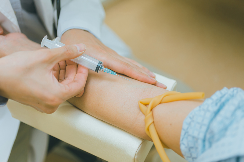 採血をするため、患者が腕を台にのせ、注射を持つ医師の手のイメージ写真