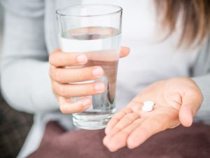 Closeup woman hand with pills medicine tablets and glass of water for headache treatment. Healthcare, medical supplements concept