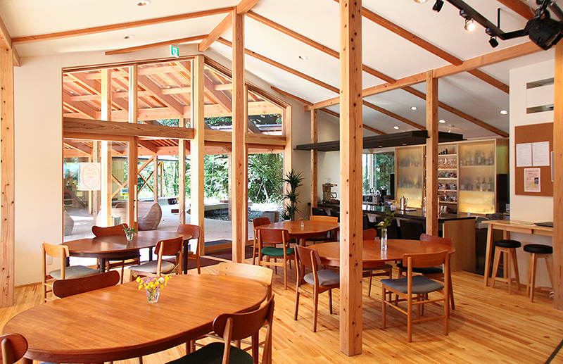 木の柱、白い壁、木目の美しいテーブルセットの並ぶカフェ