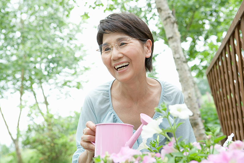 高齢女性が微笑みながら、庭で花に水やりをしている写真