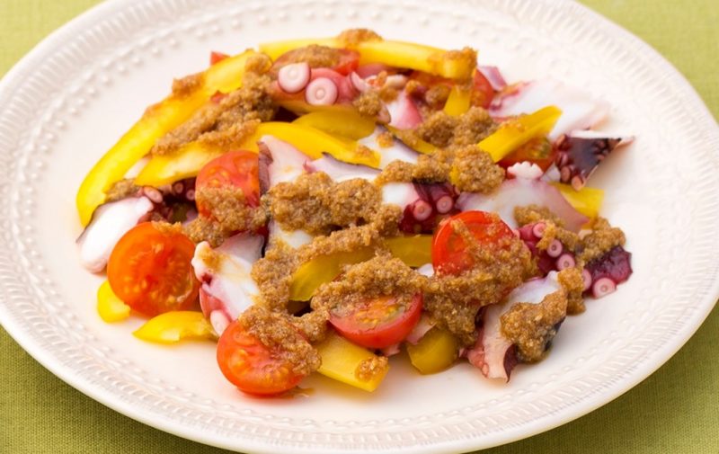 黄色いパプリカとプチトマトが華やかなタコのマリネサラダが白い器に盛りつけられている