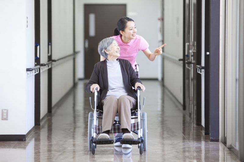 高齢女性の乗った車椅子を押す介護施設の女性