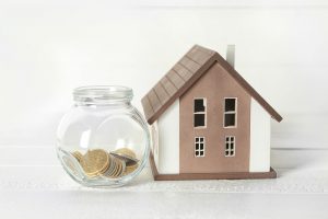 House model and glass jar with coins on white table. Mortgage concept