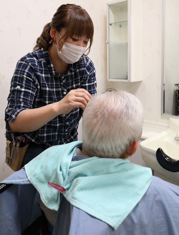 高齢者の男性のヘアカットをする美容師の女性