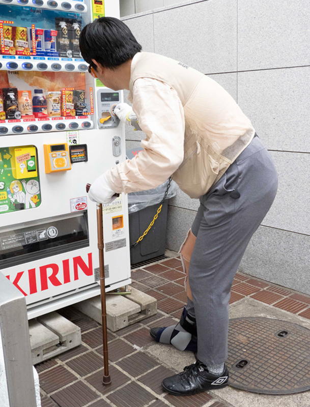 うらしま太郎を装着して、飲み物の自動販売機を利用する記者