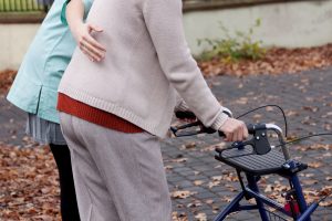 Nurse helping elder person to walk with walker