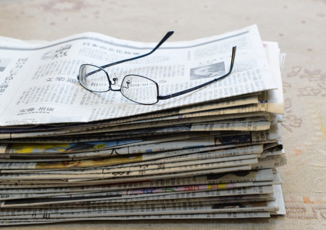 積み重ねられた新聞と、その上に乗ったメガネの写真