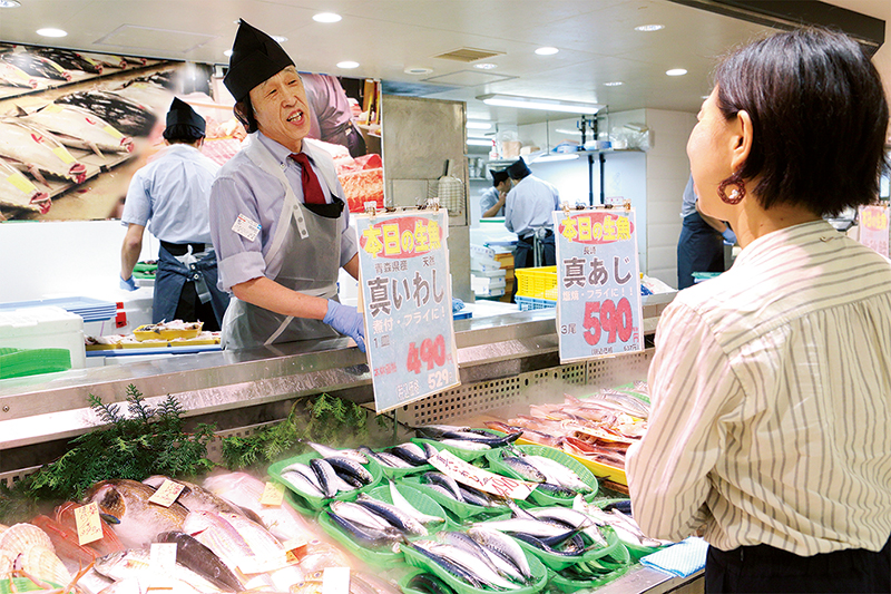 鮮魚売り場で店員さんに本日オススメの魚を聞く女性の写真