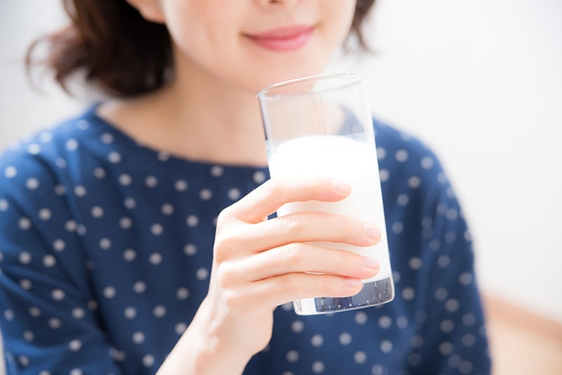 牛乳の入ったグラスを片手に持つ女性の写真
