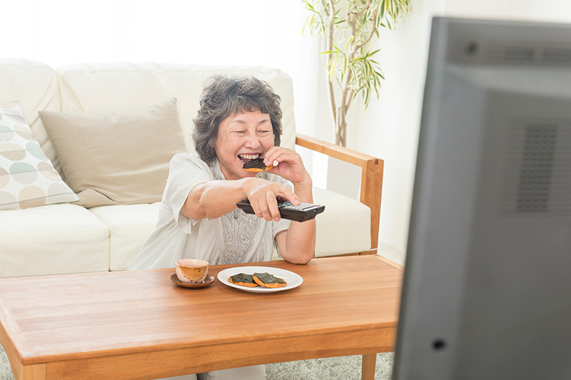 せんべいを食べながらテレビを見るシニア女性