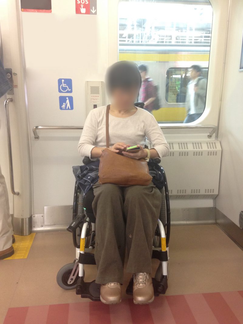 電車の中で車椅子に乗りスマホを操作する女性