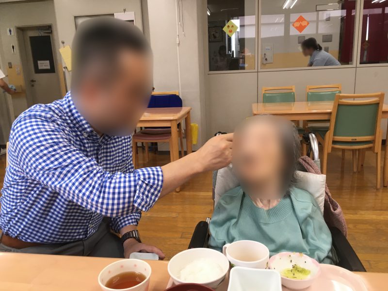 車椅子に座る高齢女性の食事の介助をする男性