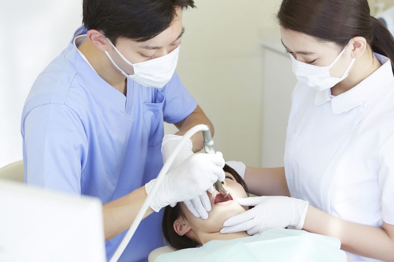 診察台で歯科医と衛生士に口腔内を診察されている女性