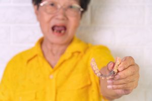 Asian Elderly woman over 70 years old be smile with a few broken teeth and holding dentures in hand. Dentures for prosthetic devices constructed to replace missing teeth and helping to chew food.