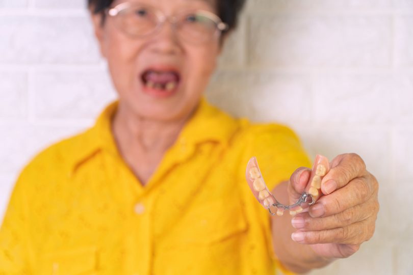 Asian Elderly woman over 70 years old be smile with a few broken teeth and holding dentures in hand. Dentures for prosthetic devices constructed to replace missing teeth and helping to chew food.