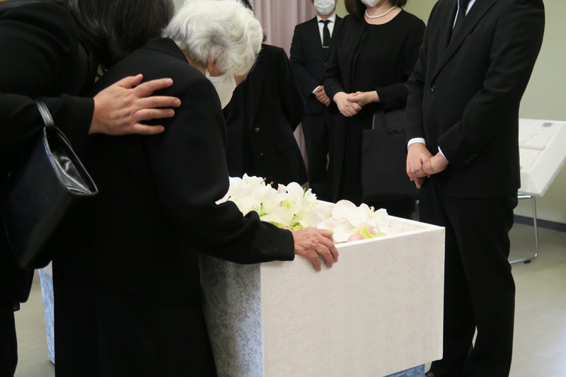 葬儀で棺桶を見つめるマスクをした高齢の女性