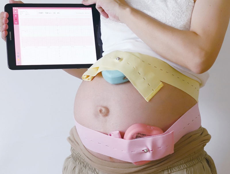 お腹に計測器を巻いて手にiPadを持つ妊婦のウエスト画像
