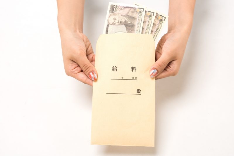 給料袋に入った１万円札３枚を持つ女性の手