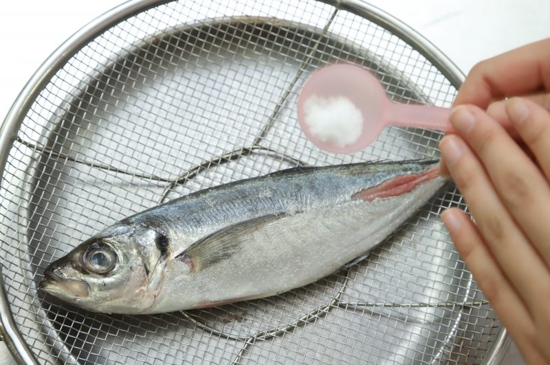 皿の上に置いたザルに魚を寝かせ、一尾の場合は魚の重さの2％、切り身の場合は1％の塩を両面にまんべんなく振る