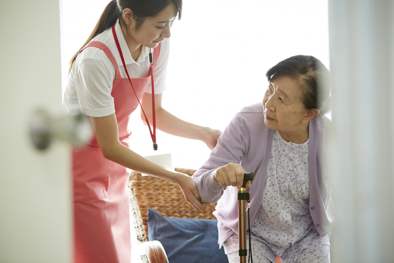 杖をつく高齢者を支える介護職の女性
