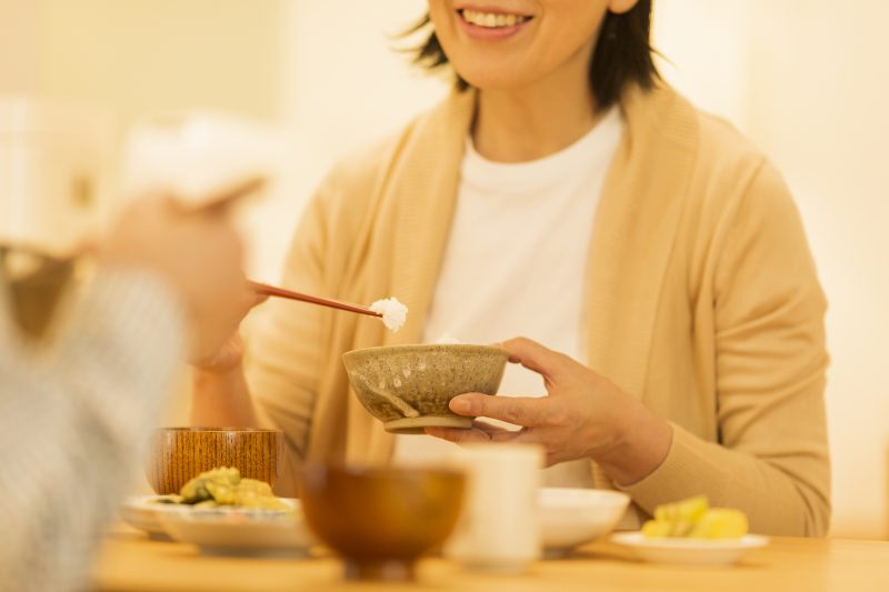 ご飯茶碗を手に持ち食事をする女性
