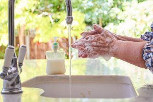 Senior woman washing her hands at the sink with liquid soap and water from the tap in the kitchen at home