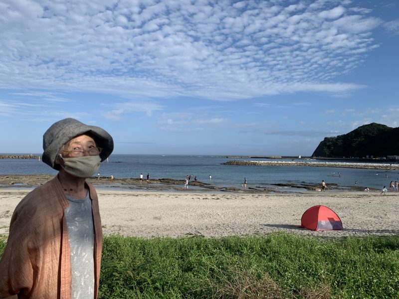 海辺に立つ、マスクをした飯田裕子さんの母