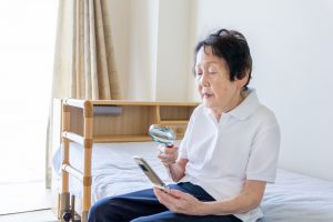 Asian senior woman reading the letter on the phone with magnifying glass