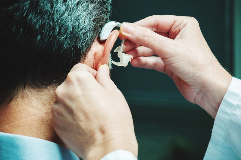 男性の耳に補聴器をセットしている画像