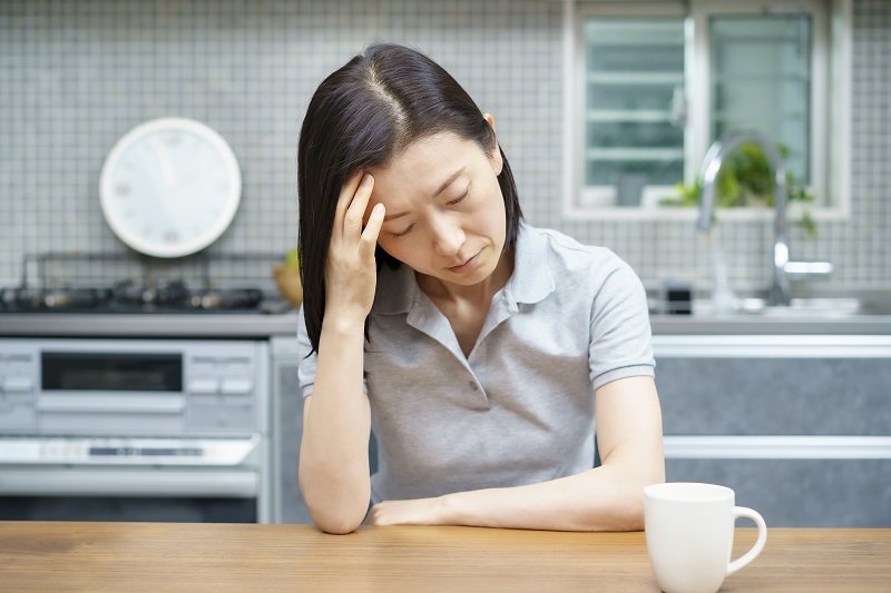 食卓で頭を抑える女性