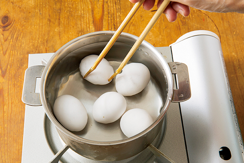 鍋に入れた卵を菜箸で転がしている