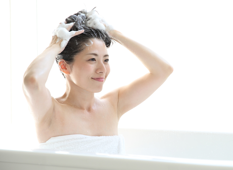 お風呂につかりシャンプーする女性の画像