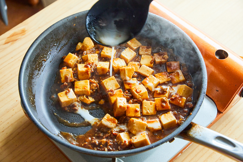 フライパンで合わせた調味料と豆腐に水溶き片栗粉を注いでいる写真