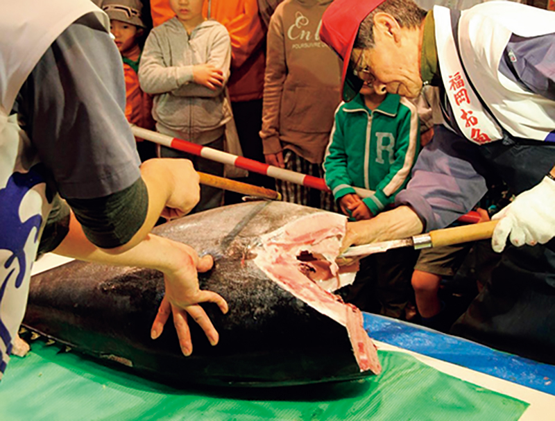 市場で巨大な魚に包丁を入れる画像