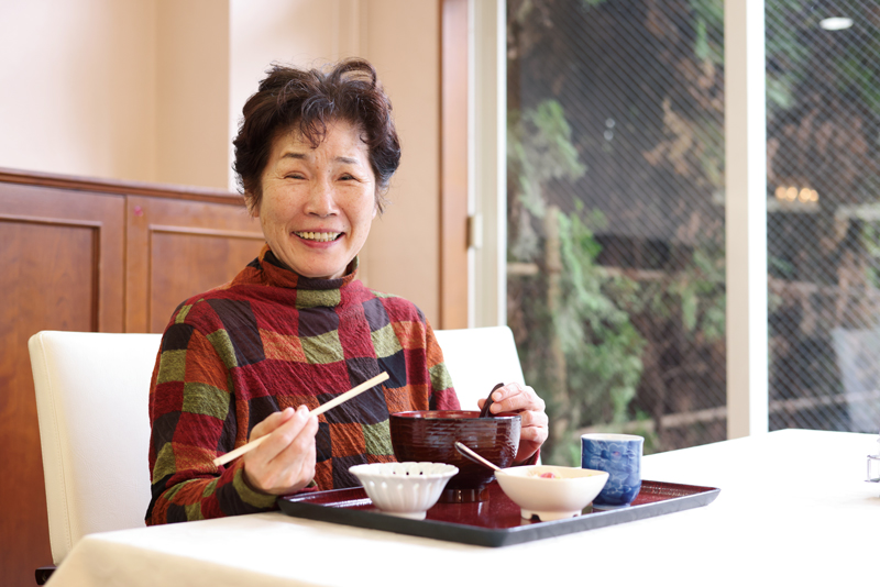 高齢者ホームのダイニングレストランでうどんを食べる女性