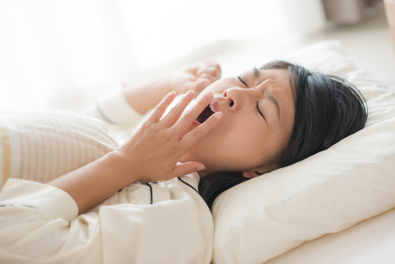 ベッドで横になりあくびをする女性