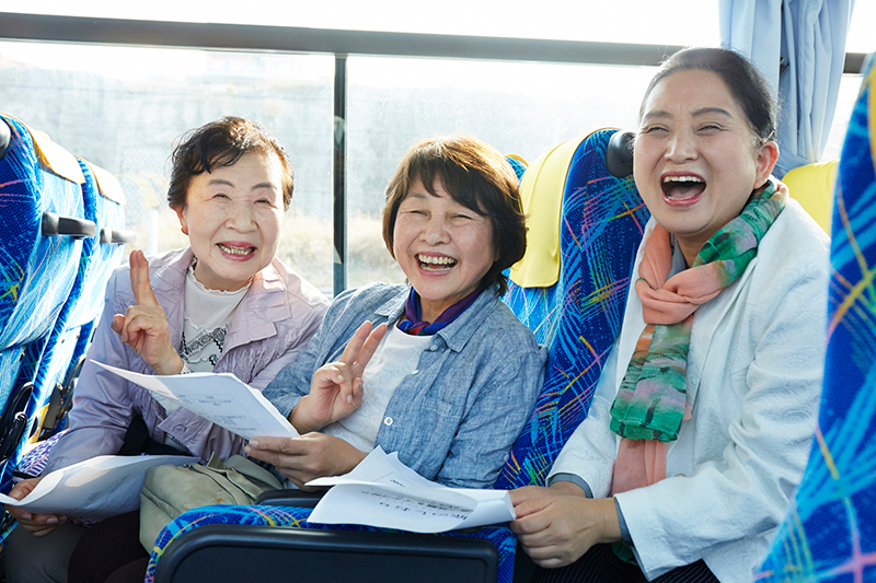 バスの中で笑顔でピースをする3人のシニア女性