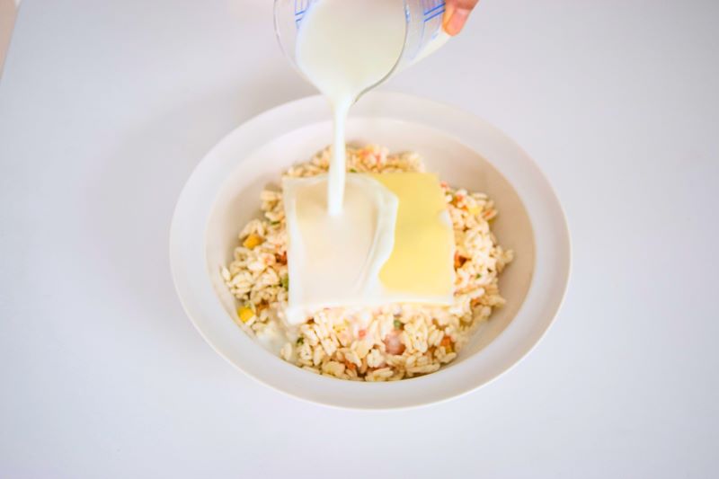 お皿の冷凍エビピラフにスライスチーズ1枚をのせて牛乳を注いでいる写真