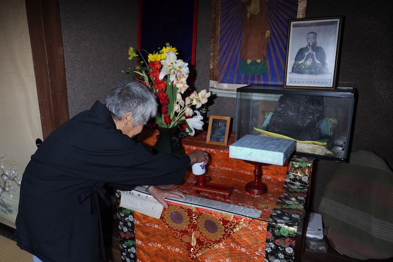 床の間には、飛龍山を開山した始祖・萬治さんの遺影と焼け残った木像が祀られる。ここでキミさんは深々と頭を下げる