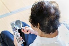 Asian senior woman reading the letter on the phone with magnifying glass